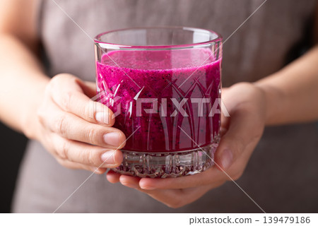 Glass of red dragon fruit smoothie holding by woman hand, Healthy tropical summer drink Glass of red dragon fruit smoothie holding by woman hand, Healthy tropical summer drink 139479186
