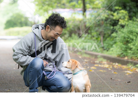 A man who owns a beagle, a smiling portrait of him walking his dog, a lifestyle of living with animals. 139479704