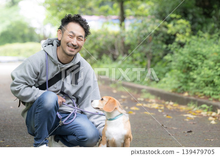一位擁有比格犬的男士,一張他牽著狗狗散步的微笑照片,一種與動物共同生活的生活方式。 一位擁有比格犬的男士,一張他牽著狗狗散步的微笑照片,一種與動物共同生活的生活方式。 139479705