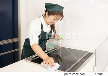 A woman working as a house cleaner wipes down an induction cooktop. 139479853