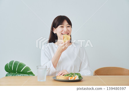 Smiling young woman enjoying breakfast Smiling young woman enjoying breakfast 139480397
