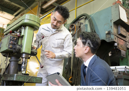 A worker and salesperson explaining the maintenance of manufacturing machinery, the purchase of new machinery (capital investment), and financing. 139481051
