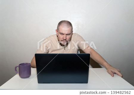 Man peers anxiously and attentively at a laptop monitor, focusing with intensity on a screen 139482562