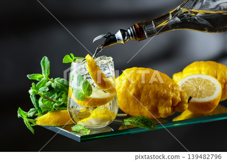 In glass with lemon wedges, ice cubes and mint leaves is poured string alcohol. In glass with lemon wedges, ice cubes and mint leaves is poured string alcohol. 139482796
