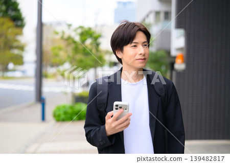 A young businessman with his eyes closed, holding his smartphone. A young businessman with his eyes closed, holding his smartphone. 139482817