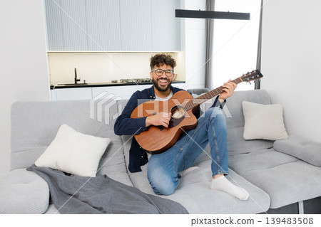 Happy man playing acoustic guitar on sofa Happy man playing acoustic guitar on sofa 139483508