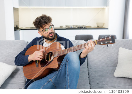 Man playing acoustic guitar and singing on sofa Man playing acoustic guitar and singing on sofa 139483509