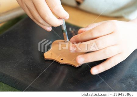A photograph of a child's hand holding a leather crafting stamp. 139483963