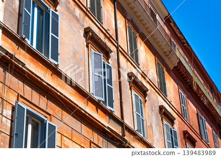 Italy Rome street orange house wall facade. Old historical building architecture in the city center. Italian windows with shutters. Italy Rome street orange house wall facade. Old historical building architecture in the city center. Italian windows with shutters. 139483989