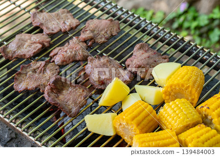 A barbecue scene of meat and corn being grilled over charcoal. A barbecue scene of meat and corn being grilled over charcoal. 139484003