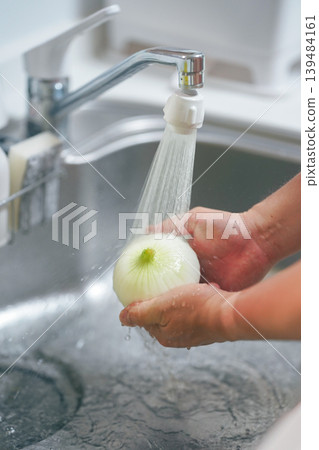 Hands of a person washing onions in the kitchen Hands of a person washing onions in the kitchen 139484161