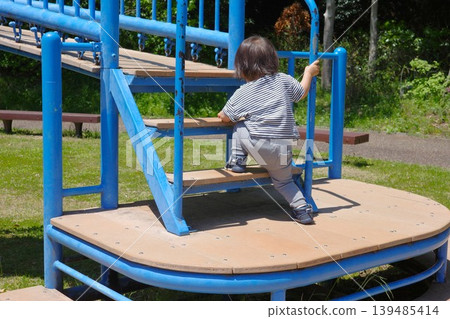 一個孩子正爬上公園裡藍色遊樂設施的台階,這是他的背影。 一個孩子正爬上公園裡藍色遊樂設施的台階,這是他的背影。 139485414