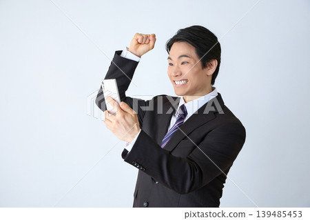 Office worker makes a fist pump while looking at his smartphone Office worker makes a fist pump while looking at his smartphone 139485453
