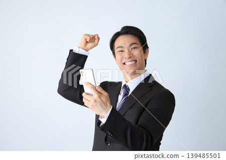 一名商人一邊舉著手機一邊歡呼。 一名商人一邊舉著手機一邊歡呼。 139485501