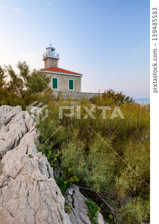 Stone lighthouse on rocky coastal hillside at dusk Stone lighthouse on rocky coastal hillside at dusk 139485583