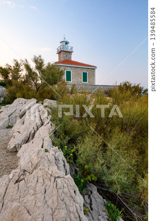 Stone lighthouse on rocky coastal hillside at dusk Stone lighthouse on rocky coastal hillside at dusk 139485584