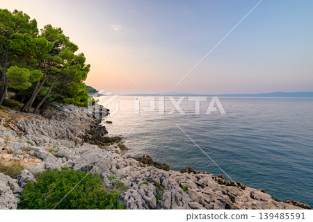 Tranquil rocky coastline at sunset with calm sea Tranquil rocky coastline at sunset with calm sea 139485591
