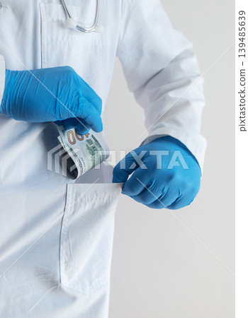 Close-up of doctor in white coat and blue gloves receiving or hiding cash. Concept of high medical salary, corruption in medicine, healthcare bribery, and expensive health insurance. Close-up of doctor in white coat and blue gloves receiving or hiding cash. Concept of high medical salary, corruption in medicine, healthcare bribery, and expensive health insurance. 139485639