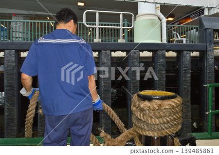 Dock worker on ferry deck handling thick mooring ropes at a Star ferry harbor terminal in Hong Kong, China Dock worker on ferry deck handling thick mooring ropes at a Star ferry harbor terminal in Hong Kong, China 139485861