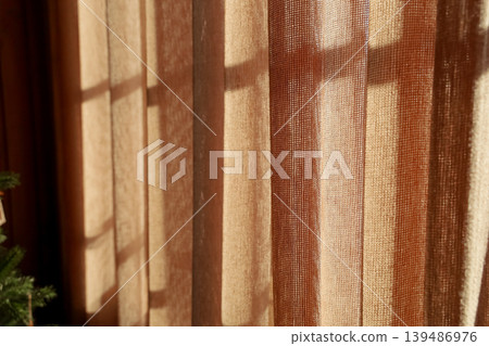 Sunlight filters through sheer curtains in a warm room creating patterns on the wall. Sunlight filters through sheer curtains in a warm room creating patterns on the wall. 139486976