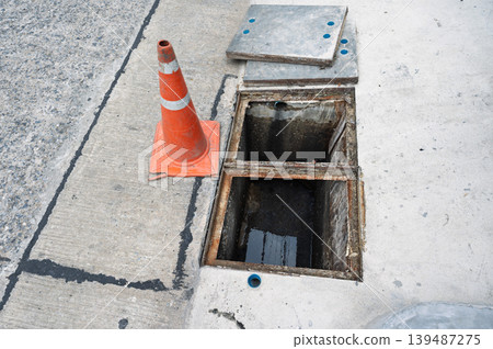 Dangerous open drain hole on concrete street with orange caution cone Dangerous open drain hole on concrete street with orange caution cone 139487275