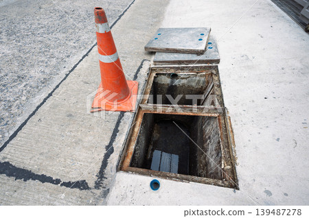 Open street drain sewer hole with warning orange traffic cone for dangerous alert Open street drain sewer hole with warning orange traffic cone for dangerous alert 139487278