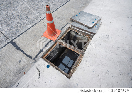 Scary open manhole hazard with orange traffic cone on concrete street Scary open manhole hazard with orange traffic cone on concrete street 139487279