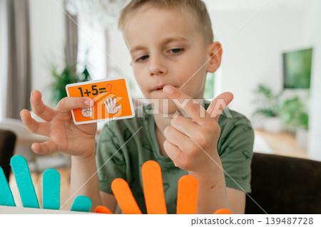 Young boy learning basic math by counting on his fingers at home. The scene highlights early childhood education and cognitive development in a comfortable Young boy learning basic math by counting on his fingers at home. The scene highlights early childhood education and cognitive development in a comfortable 139487728