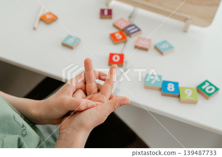 Child counting numbers using fingers during a learning session. The activity supports early math skills and cognitive development. Child counting numbers using fingers during a learning session. The activity supports early math skills and cognitive development. 139487733