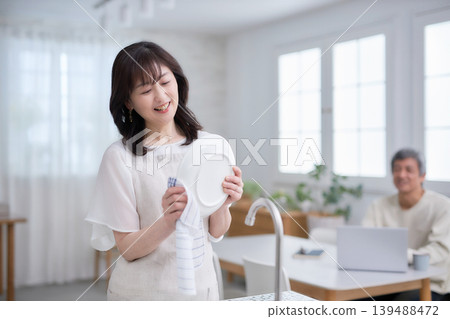 A man and woman in their 60s smiling and talking while wiping dishes in the kitchen A man and woman in their 60s smiling and talking while wiping dishes in the kitchen 139488472