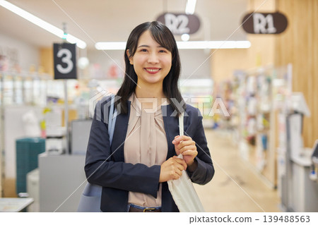 A young woman finishes paying at a self-checkout and slings her eco-bag over her shoulder. 139488563
