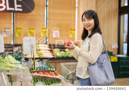 一位年輕女子在超市購物時一邊看著她的智慧型手機。 一位年輕女子在超市購物時一邊看著她的智慧型手機。 139488642