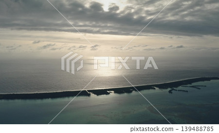 Sunlight reflects calm ocean water near tropical island with overwater bungalows, creating beautiful serene scene under cloudy sunset sky. Exotic travel vacation getaway background. Drone flight Sunlight reflects calm ocean water near tropical island with overwater bungalows, creating beautiful serene scene under cloudy sunset sky. Exotic travel vacation getaway background. Drone flight 139488785