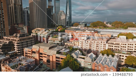 Australia, Sydney City: modern downtown skyscrapers and historic low-rises buildings houses under bright cloudy sky, highlighting urban development. Drone flight aerial view Australia, Sydney City: modern downtown skyscrapers and historic low-rises buildings houses under bright cloudy sky, highlighting urban development. Drone flight aerial view 139488793