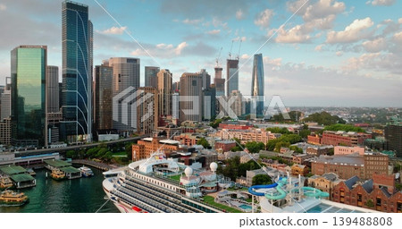 Sydney skyline aerial view urban cityscape. Modern skyscrapers buildings and large cruise ship docked at bustling Circular Quay harbor. Contrasting new and old architecture under bright evening sky Sydney skyline aerial view urban cityscape. Modern skyscrapers buildings and large cruise ship docked at bustling Circular Quay harbor. Contrasting new and old architecture under bright evening sky 139488808