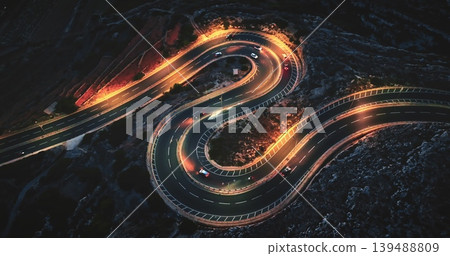 Malta: Aerial view winding road at night, with illuminated cars creating mesmerizing light trails against the dark landscape. Drone flight Malta: Aerial view winding road at night, with illuminated cars creating mesmerizing light trails against the dark landscape. Drone flight 139488809