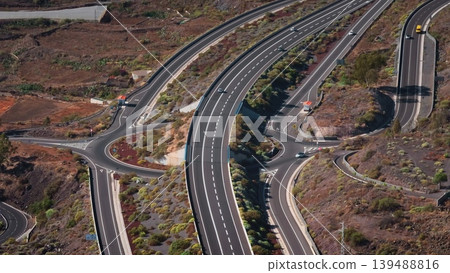 Tenerife, Canary Islands: Aerial view highway traffic road intersection and roundabout weaving through the volcanic landscape near Teide National Park in Tenerife. Drone flight 139488816