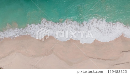 Top down turquoise ocean waves breaking shore, white foam crashing pristine, light colored sand of a picturesque tropical beach on the tropical Lombok island, Indonesia. Aerial view natural bavkground 139488823