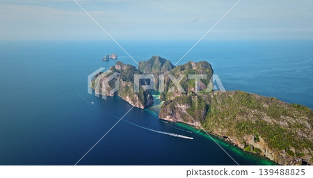 Tropical Phi Phi island displaying lush green limestone cliffs rising from turquoise water with boat cruising past, offering a stunning travel destination and vacation landscape. Aerial drone panorama Tropical Phi Phi island displaying lush green limestone cliffs rising from turquoise water with boat cruising past, offering a stunning travel destination and vacation landscape. Aerial drone panorama 139488825