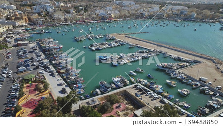 Malta: Drone capturing the vibrant Luzzu boats of Marsaxlokk Harbour, blending Maltese maritime heritage with modern yachts and a bustling cityscape. Drone flight Malta: Drone capturing the vibrant Luzzu boats of Marsaxlokk Harbour, blending Maltese maritime heritage with modern yachts and a bustling cityscape. Drone flight 139488850