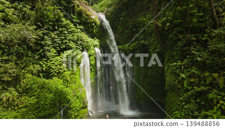Sendang Gile waterfall cascading into a lush tropical rainforest. Surrounded by vibrant green vegetation. With people standing in the refreshing natural pool. Highlighting peace and nature beauty 139488856