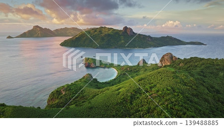 Fiji, Yasawa tropical Islands with lush green mountains hills, white beach and calm turquoise lagoon water under vibrant sunset sky, idyllic South Pacific paradise. Aerial view drone flight panorama Fiji, Yasawa tropical Islands with lush green mountains hills, white beach and calm turquoise lagoon water under vibrant sunset sky, idyllic South Pacific paradise. Aerial view drone flight panorama 139488885