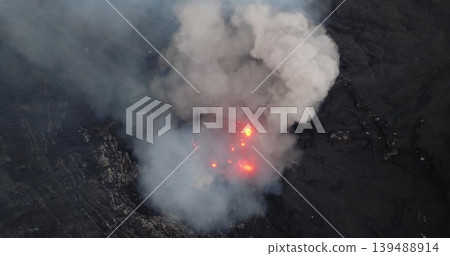 Mount Yasur volcano erupting from an aerial drone viewpoint, showing molten lava explosions and thick smoke rising from the active crater in a dramatic display of raw power and natural hazard 139488914