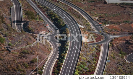 Tenerife, Canary Islands: Aerial view capturing cars driving along highway TF-1 through Tenerife's volcanic terrain, highlighting scenic infrastructure. Drone flight Tenerife, Canary Islands: Aerial view capturing cars driving along highway TF-1 through Tenerife's volcanic terrain, highlighting scenic infrastructure. Drone flight 139488934