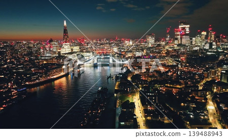 England, London: Breathtaking aerial view of night London city with Tower Bridge, The Shard, and other landmarks in colorful bright lights creating a stunning cityscape skyline under sunset sky England, London: Breathtaking aerial view of night London city with Tower Bridge, The Shard, and other landmarks in colorful bright lights creating a stunning cityscape skyline under sunset sky 139488943