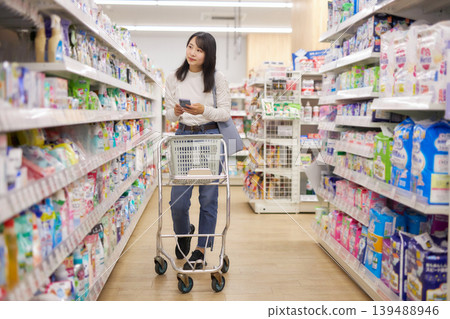 A young woman shopping at a supermarket while looking at notes on her smartphone. A young woman shopping at a supermarket while looking at notes on her smartphone. 139488946