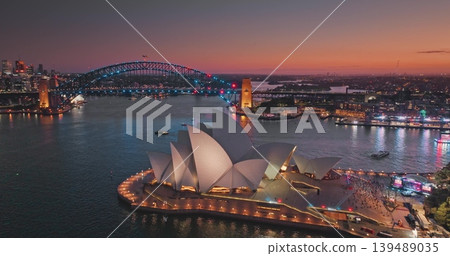Australia, Sydney: Sydney Opera House and Harbour Bridge glowing at sunset, with city lights reflecting in the water, creating a magical urban landscape. Night modern cityscape. Drone flight Australia, Sydney: Sydney Opera House and Harbour Bridge glowing at sunset, with city lights reflecting in the water, creating a magical urban landscape. Night modern cityscape. Drone flight 139489035