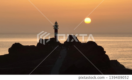 Tourists enjoy Punta de Teno Lighthouse at sunset in Tenerife, Canary Islands, Spain. Rocky landscape silhouette bright orange sky. Travel destination. Nature background. Drone flight panorama Tourists enjoy Punta de Teno Lighthouse at sunset in Tenerife, Canary Islands, Spain. Rocky landscape silhouette bright orange sky. Travel destination. Nature background. Drone flight panorama 139489052