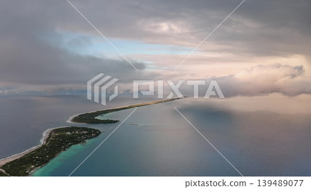 Breathtaking aerial view of Rangiroa Atoll partially covered by clouds during colorful sunset, showcasing the turquoise lagoon, lush vegetation, and surrounding ocean in French Polynesia. Drone flight 139489077