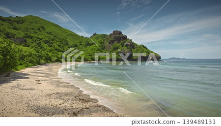 Fiji tropical island coastline pristine sandy beach, clear turquoise ocean waves, backed by dense green tropical mountains and a distant island under a blue sky. Nature paradise. Drone flight footage Fiji tropical island coastline pristine sandy beach, clear turquoise ocean waves, backed by dense green tropical mountains and a distant island under a blue sky. Nature paradise. Drone flight footage 139489131